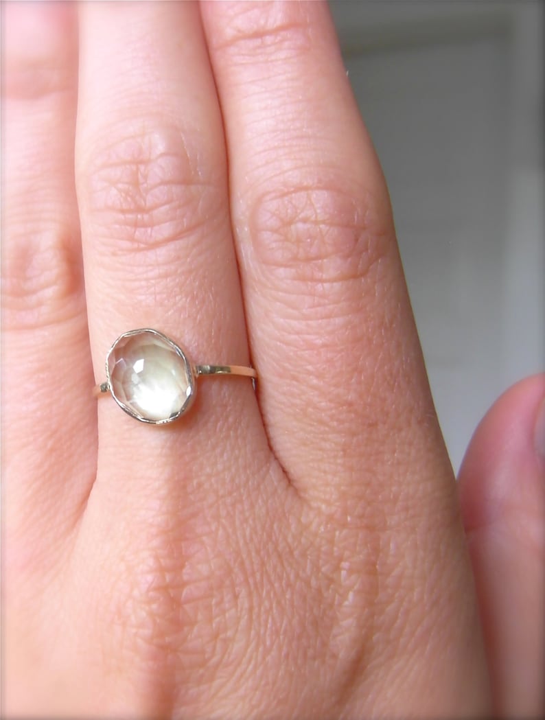 Op de afbeelding: Een gouden ring met een lichtgroene ovale edelsteen. De ring zit aan een vinger.