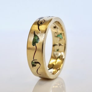 May include: A gold band ring with a design of green hearts and swirls. The ring is polished and has a smooth finish.
