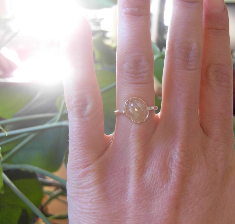 Op de afbeelding: Een gouden ring met een heldere, ovale edelsteen. De edelsteen heeft een lichtbruine kleur en is gezet in een eenvoudige band.