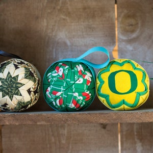 May include: Three handmade fabric ornaments, one with a green and white star pattern, one with a green and red Christmas pattern, and one with a yellow background and a green "O" in the center.
