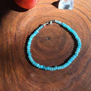 Könnte beinhalten: Ein blaues Edelstein-Armband mit einem silbernen Verschluss. Das Armband besteht aus kleinen, runden Perlen und liegt auf einer Holzoberfläche.