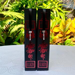 May include: Two black boxes with red rose designs and silver charms. The boxes have the text "HD CARLTON" printed on the bottom.