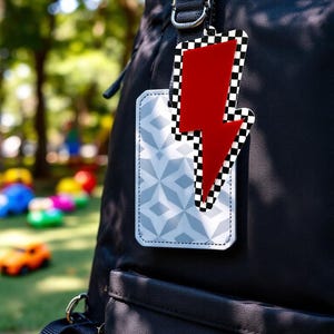 May include: A black backpack with a decorative tag featuring a red lightning bolt design with a black and white checkered border. A second tag with a geometric pattern is also attached.