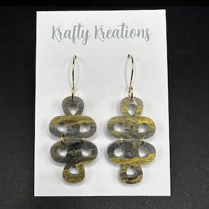 May include: A pair of dangle earrings with a gold and gray marbled design. The earrings are in a unique shape with multiple connected loops. The earrings hang from gold-colored ear wires. The earrings are displayed on a white card with the text "Krafty Kreations".