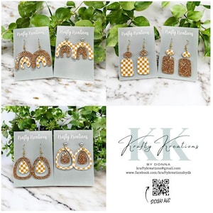May include: A collection of handmade earrings displayed on gray cards. The earrings feature various designs, including arches, rectangles, and teardrops, with gold glitter and checkered patterns in white and mustard yellow. The brand name "Krafty Kreations" is visible.