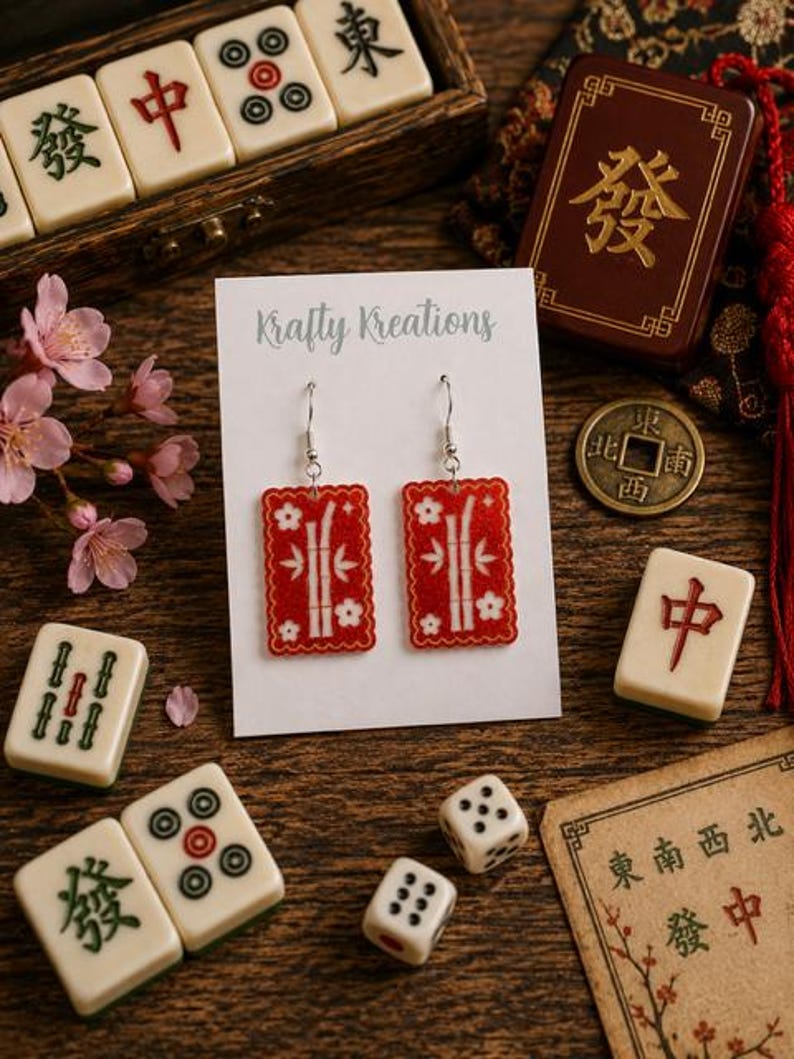 May include: Red rectangular earrings with white bamboo and flower designs are displayed on a white card that reads "Krafty Kreations." The image includes Mahjong tiles, dice, and a small wooden box with Chinese characters.