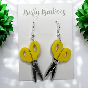 Peut inclure: Une paire de boucles d'oreilles en forme de ciseaux jaunes avec des crochets argentés. Les boucles d'oreilles sont en acrylique et ont une finition miroir.