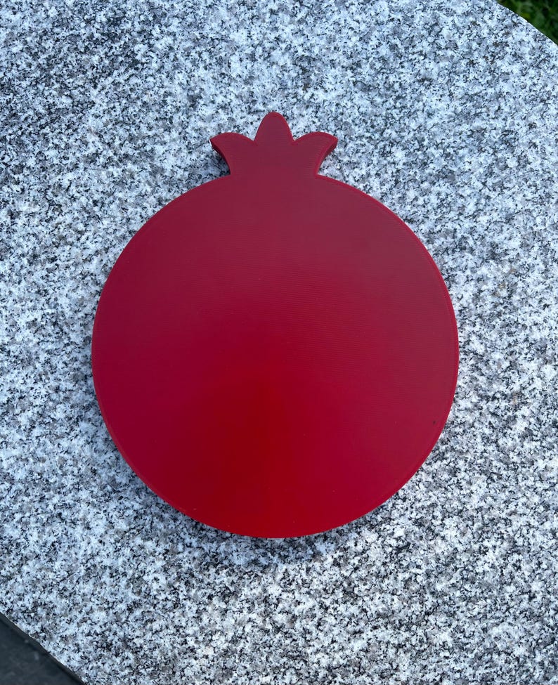 May include: A red wooden pomegranate shaped cutting board.