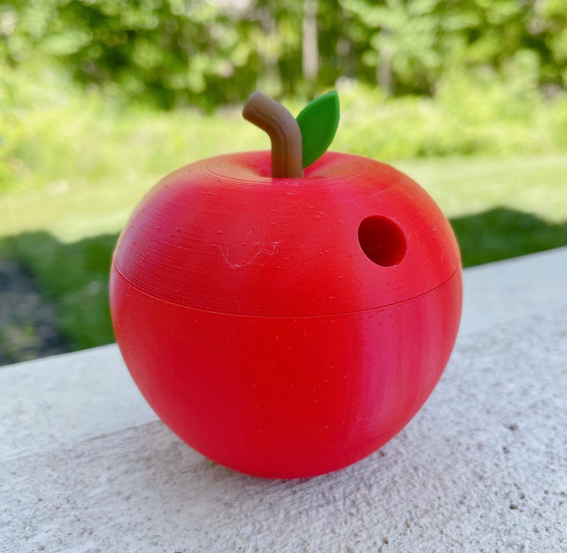K&ouml;nnte beinhalten: Ein roter, apfelf&ouml;rmiger Bleistifthalter mit einem gr&uuml;nen Blatt und einem braunen Stiel. Der Halter hat oben ein Loch f&uuml;r Bleistifte.