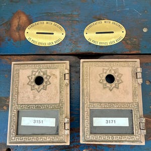 May include: Two vintage US Post Office lock boxes with brass plates that read "Handcrafted with Original US Post Office Lock Boxes." The boxes are tan with a decorative border and a starburst design. One box reads "3151" and the other reads "3171."