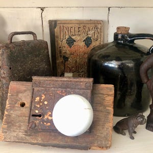 May include: A collection of vintage items including a wooden door knob, a metal cowbell, a black ceramic jug, a wooden sign with the text "Uncle Sam's", and a cast iron figurine of a man.