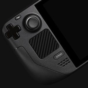 May include: A black handheld gaming device with a black and white carbon fiber design, a circular button, a cross-shaped button, and a "STEAM" button.