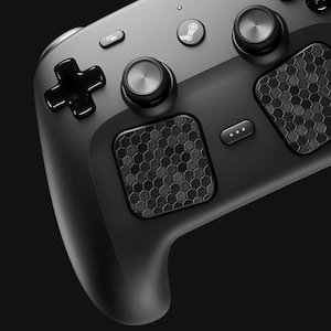 May include: A matte black video game controller featuring two circular trackpads with a textured hexagonal pattern, two analog sticks with metallic silver tops, a glossy black directional pad, and a central button with a Steam logo icon.