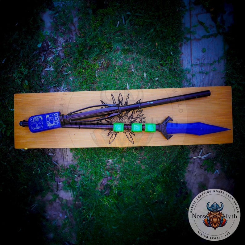 May include: A blue and black spear with a wooden handle and green accents. The spear is displayed on a wooden board with the text "Battle Crafting Horse Saga Shield Norse Myth Viking Legacy Art".
