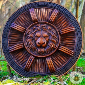 May include: A round wooden shield with a carved lion's head in the center. The shield is decorated with a black and white Greek key pattern around the edge.