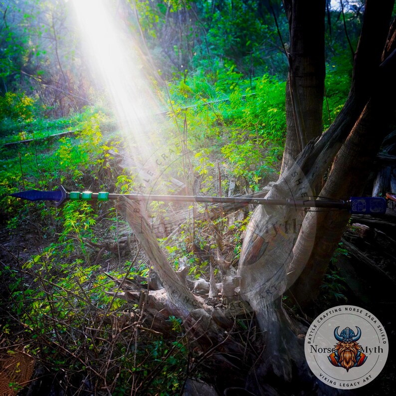 May include: A wooden spear with a blue and green tip, resting on a tree trunk in a forest setting. The spear is decorated with a green and blue band. The image includes the text "Battle Crafting Horse Saga Shield Norse Myth Viking Legacy Art".