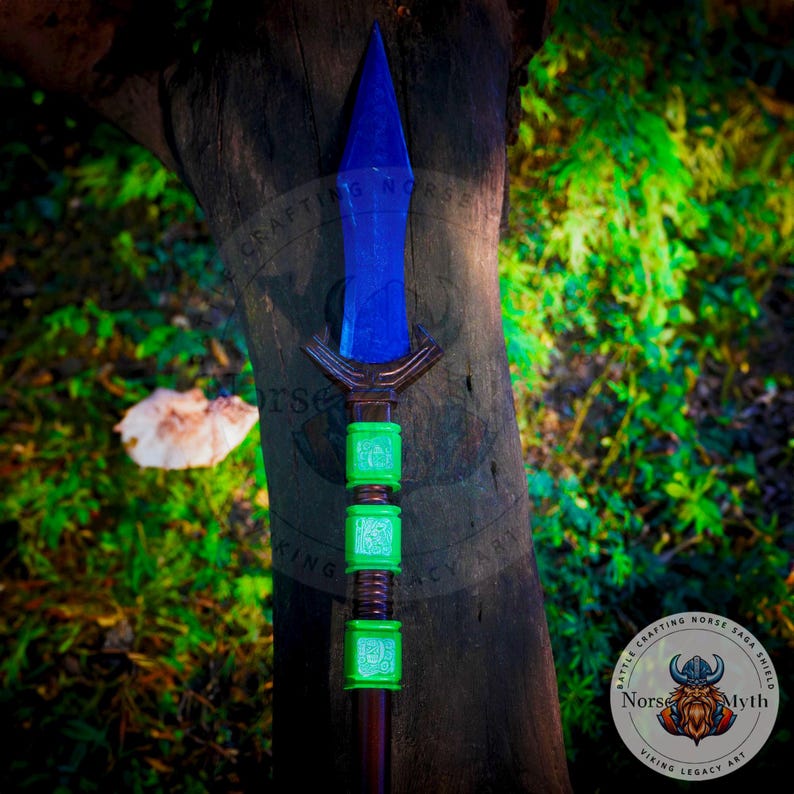 May include: A blue and green spear with a wooden shaft and a blue metal tip. The spear has green rings with runes on them. The spear is leaning against a tree trunk. The text on the image reads "Battle Crafting Norse Saga Shield Norse Myth Viking Legacy Art."