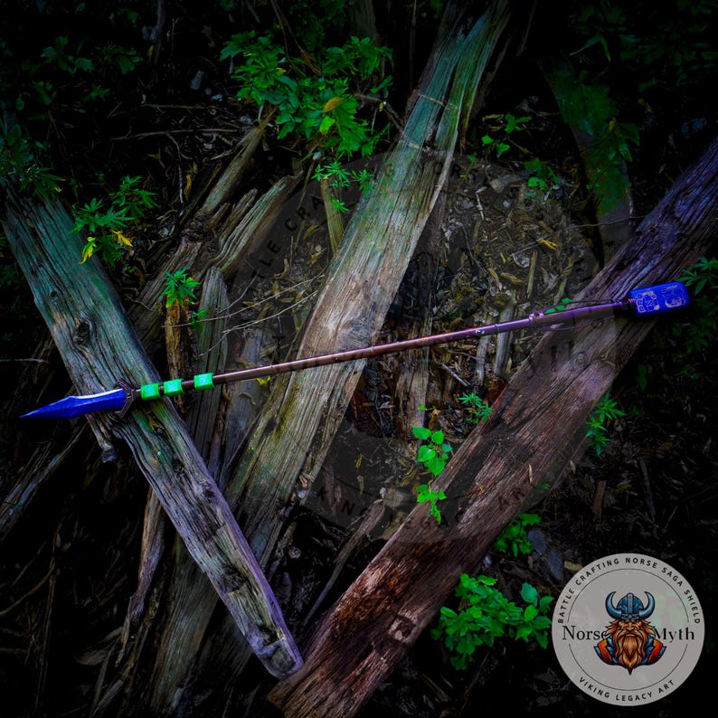 May include: A blue and green spear with a wooden shaft, lying on a bed of weathered wooden planks. The spear has a decorative design on the tip and a green and blue band near the handle. The spear is surrounded by green foliage.