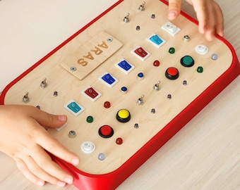 May include: A wooden toy panel with red trim and various switches, buttons, and lights. The panel is labeled "ARAS".