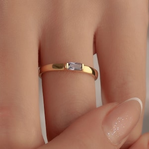 Peut inclure: Une bague en or avec une pierre précieuse rectangulaire de couleur claire au centre. La bague est simple et élégante, avec une finition polie. La bague est portée au doigt.