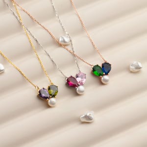 May include: A collection of delicate necklaces with colorful gemstone pendants and a single pearl. The necklaces feature gold, silver, and rose gold chains. The pendants showcase a variety of colors, including purple, green, pink, and blue, with a pear-shaped design.