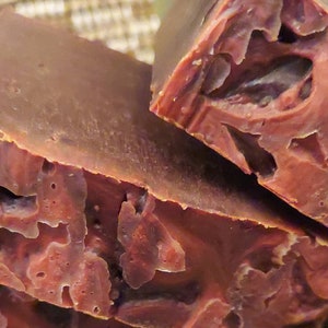 May include: Close-up of a stack of handmade soap bars. The soap bars are a deep brown colour with swirls of red and white. The soap bars are arranged in a pyramid shape.