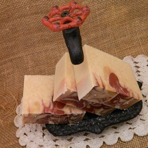 May include: Four bars of handmade soap with swirls of brown and white. The soap is displayed on a black metal soap dish with a red and black vintage water valve on top.