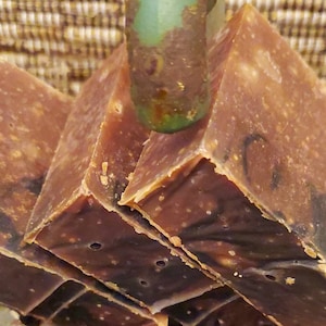 May include: Stacked bars of brown and black speckled soap with a green and brown base.