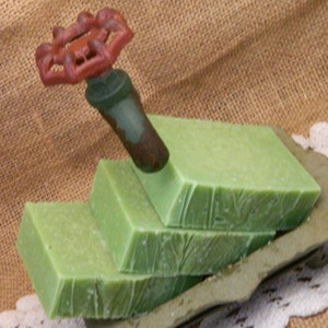 May include: Three bars of green soap stacked on top of each other. The soap is in a decorative tray. A rusty red and green metal valve is on top of the soap.
