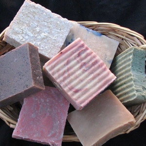 May include: A wicker basket filled with six different bars of handmade soap. The soaps are in various colors, including white, pink, brown, and green. Some of the soaps have a striped pattern.