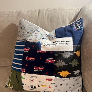 May include: A patchwork pillow made from baby clothes with a variety of patterns, including fire engines, dinosaurs, and cars. The pillow has a small embroidered heart with the text "There was always a purpose... for you to be my daddy." and a larger embroidered patch with the text "Rollin' with my Daddy".