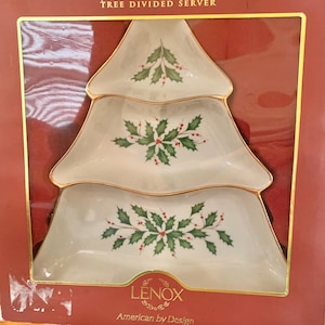 May include: A white ceramic tree-shaped divided server with gold trim, featuring holly and berry designs. The server is in its original packaging, which is red with gold lettering that reads "Holiday Tree Divided Server" and "LENOX American by Design."