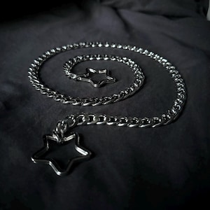 May include: A silver chain necklace with two star-shaped charms. The chain is thick and has a curb link design. The charms are simple and elegant.