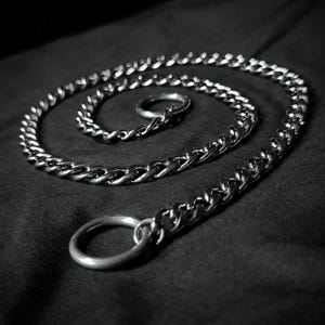 May include: A silver chain with a thick, twisted link design. The chain is coiled on a black surface and has two silver rings attached.