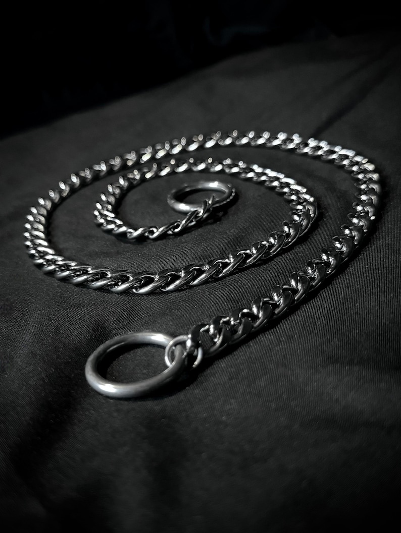May include: A silver chain with a thick, twisted link design. The chain is coiled on a black surface and has two silver rings attached.
