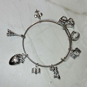 May include: Silver charm bracelet with multiple charms, such as the Eiffel Tower, a heart, a book, a camera, and theatre masks. The bracelet is circular with a clasp. The detailed charms give a personalized feel.