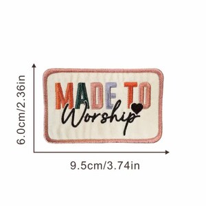 May include: Embroidered patch with the words "MADE TO Worship" in various colors, including orange, green, and blue. The patch is rectangular, measuring 3.74 inches wide and 2.36 inches high, with a pink border and a black heart.