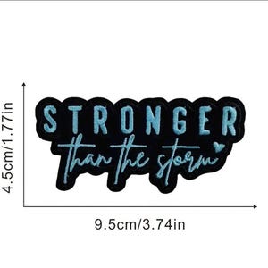May include: Black embroidered patch with the text "STRONGER than the storm" in light blue. The patch is 3.74 inches long and 1.77 inches tall. The patch has a black border and a heart symbol.