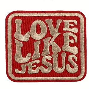 May include: A red embroidered patch with the words "LOVE LIKE JESUS" in a stylized, off-white font. The patch has a rectangular shape with rounded corners and a matching off-white border.