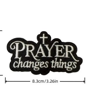 May include: Black embroidered patch with the words "PRAYER changes things" in white script. The patch is 3.26 inches wide and 1.96 inches tall, with a cross at the top. The patch has a black border.
