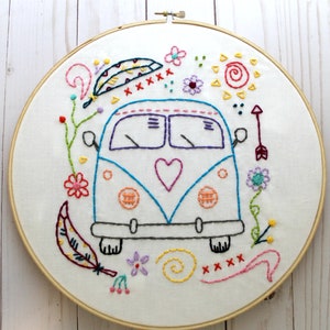 May include: Embroidered hoop art featuring a blue and white vintage van with a heart, surrounded by colorful flowers, feathers, and swirls.