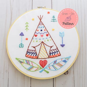 May include: Colorful embroidered hoop art featuring a teepee with hearts, arrows, and feathers. The text "Iron-On Pattern" is in a pink circle.