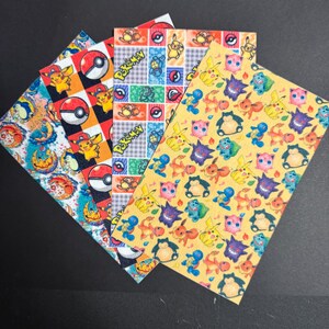 May include: Five rectangular sheets with colorful patterns featuring various Pokémon characters. Designs include Pikachu, Poké Balls, and other creatures on backgrounds of red, yellow, and blue. The sheets are arranged in a fan shape.