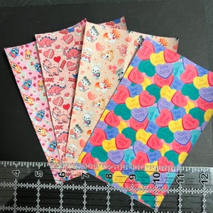 May include: Four sheets of pink and white patterned paper with hearts, animals, and candy hearts. The candy hearts have the text "Love You", "Too Cute", "Hug Me", and "Be Mine".
