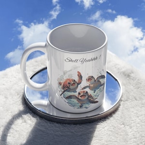 Könnte beinhalten: Eine weiße Keramiktasse mit Henkel. Die Tasse hat ein Motiv von drei Cartoon-Meeresschildkröten, die in einem Kreis schwimmen, mit dem Text "Shell Yeahhh!" auf der Tasse.