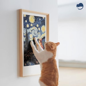 May include: A cat reaches up to scratch a framed print of a starry night painting. The cat is orange and white with a long tail. The painting is in a wooden frame.