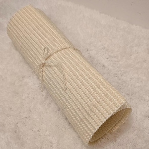 Op de afbeelding: Een witte geweven badmat opgerold op een wit pluche oppervlak.