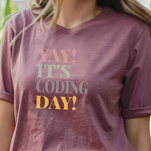 May include: A mauve t-shirt with the text "YAY! IT'S CODING DAY!" in colorful letters.