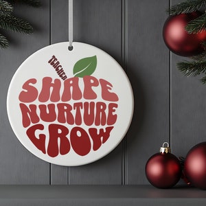 May include: A white ceramic ornament shaped like an apple with the words "Teacher Shape Nurture Grow" in red and green lettering.