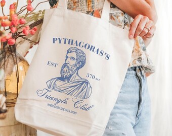 May include: Cream-colored tote bag with blue text and a graphic of Pythagoras. The text reads "PYTHAGORAS'S Triangle Club" with "EST 570 BCE" and the tagline "WHERE EVERY SIDE HAS A STORY". The bag has two handles and is held by a person.